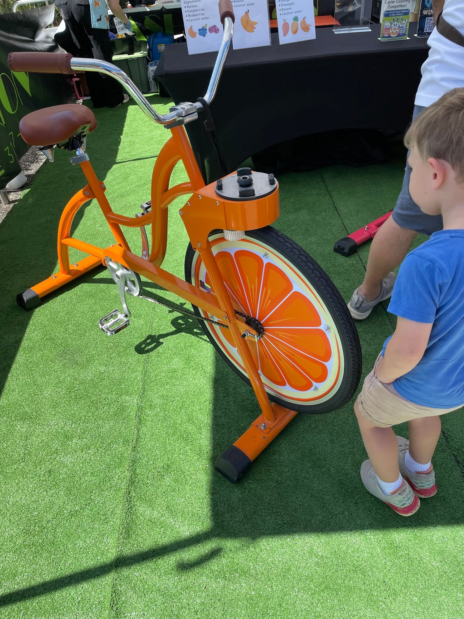 A boy looks at the orange smoothie bike on the green mat