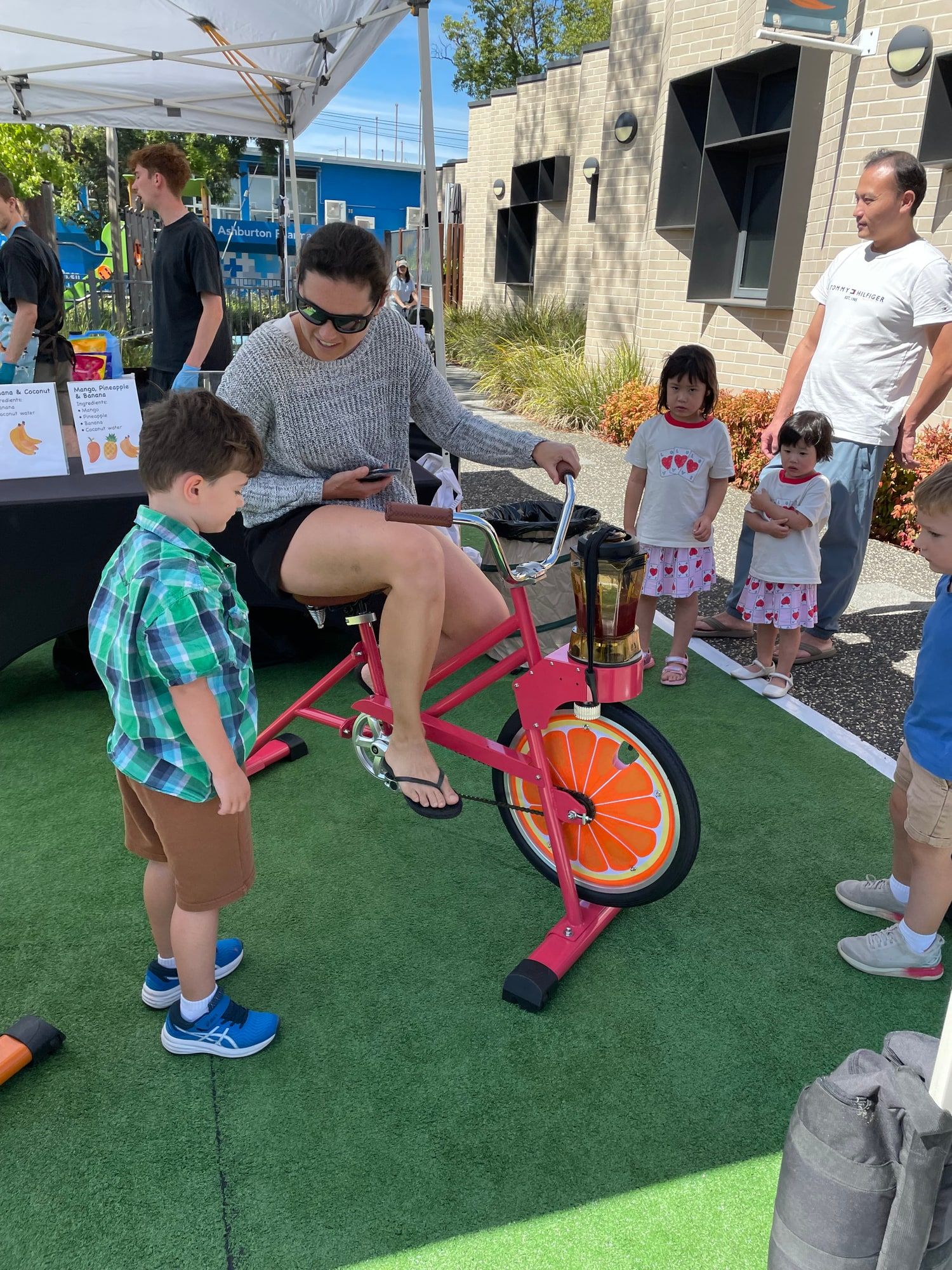An adult pedals the coral smoothie bike while children watch